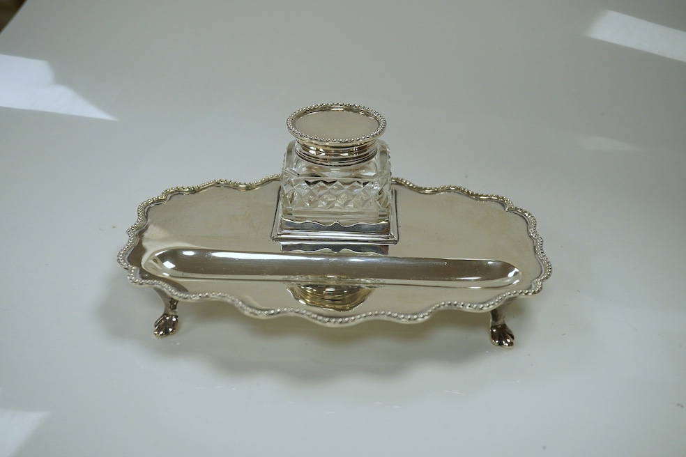 An Edwardian silver shaped oval inkstand, with wavy border, silver mounted glass well and pen recess, Skinner & Co, London, 1908, 15.8cm, together with a later engine turned silver cigarette case, 10.6oz. Condition - fai